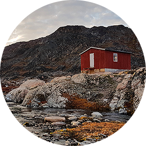Ein rotes Holzhaus steht auf den Felsen mitten in der Natur von Grönland.