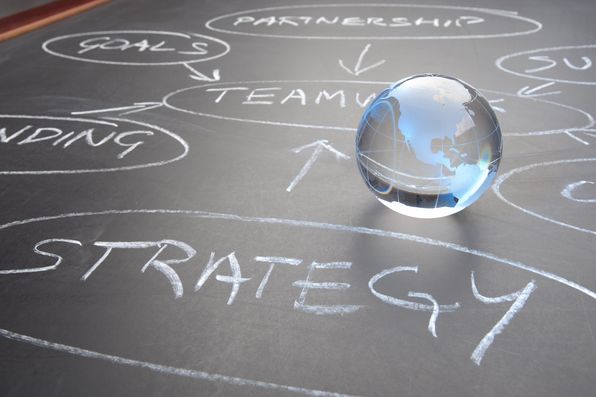 Glas-Weltkugel auf Tafel mit Stichwörtern Strategie und Teamwork